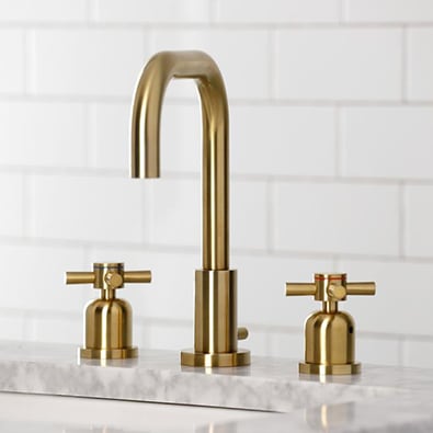 A brushed gold widespread bathroom faucet on a quartz countertop.