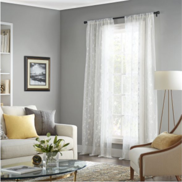 Sheer decorative curtains on a window in a light gray living room with an off-white couch.