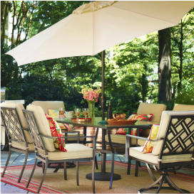 A patio dining table, 6 chairs with tan cushions and a matching tan umbrella on a patio.