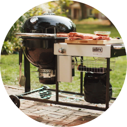 A Weber Kamado Grill loaded with ribs on a patio.