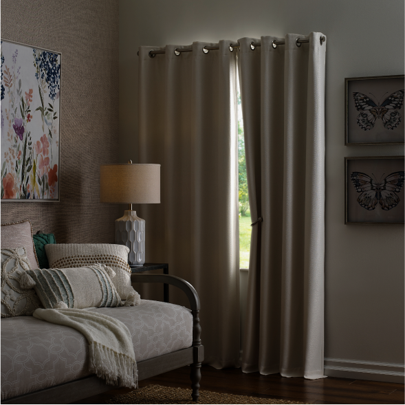 Two beige blackout curtains on a window in a room with a daybed.