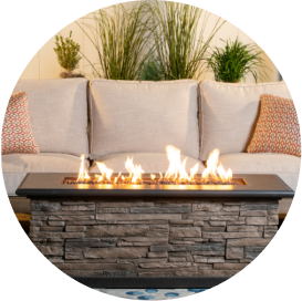 A stone fire pit table with a black top in front of a cream-colored couch.