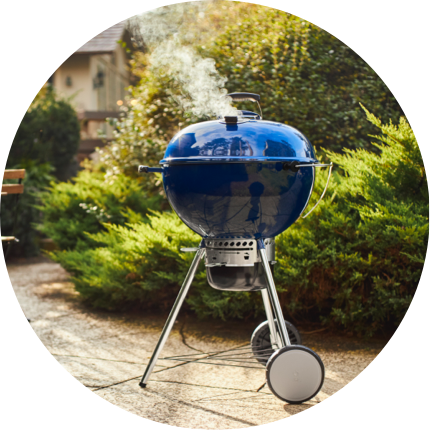 A blue Weber Master-Touch Grill on a patio with a small bistro set.