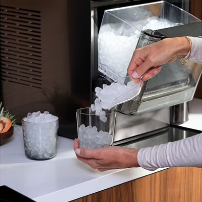 A person using an ice scoop to fill two glass tumblers with nugget ice.