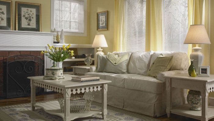 A living room with a beige couch, coffee table and end tables, yellow curtains and a fireplace.