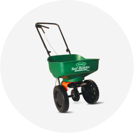 A green Scotts Turf Builder push spreader.