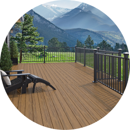 An Adirondack chair on a deck with brown Voyage decking and black railing with a view of mountains.