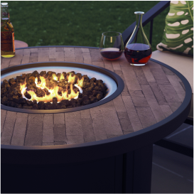 A round fire table with a fire in the center and beverages resting on the edge of the table.