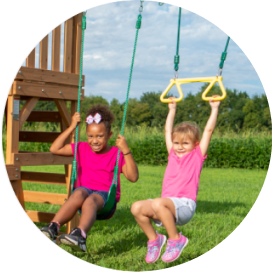 2 girls playing on a wooden swing set with a swing and trapeze rings.