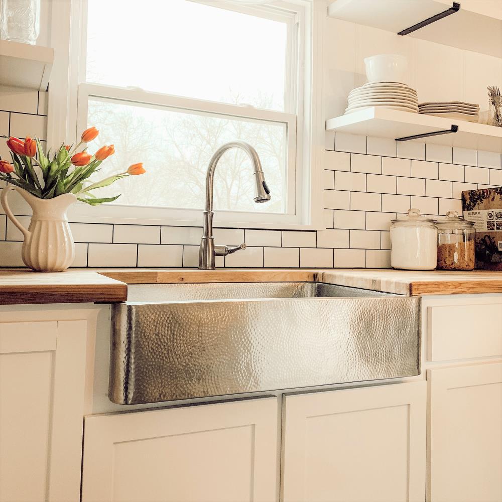 A window is located over a stainless steel apron sink paired with a deck  mount brass faucet and f…