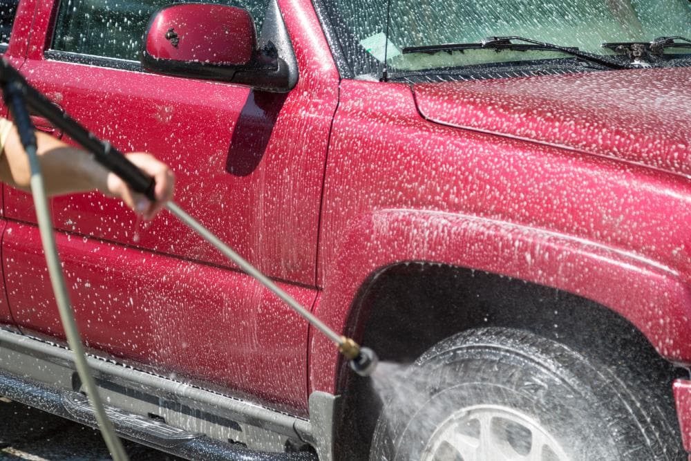 Car Wash Expert Using Water Pressure Washer to Clean a Red Modern